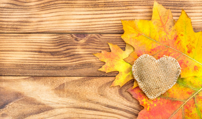 Autumn leaves with burlap heart on wooden background. Space for text.