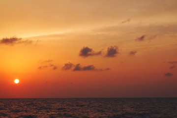 Beautiful serene view of sun setting during dusk over sea horizon with orange pastel sky 