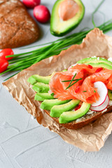 sandwich with avocado and salmon on a light background, green onions and gluten-free grain bread, radishes and tomatoes. concept diet food, copy space, sandwich take away, healthy fast food