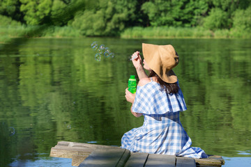 Young woman in a dress and a straw hat blowing bubbles against t