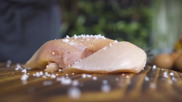 Black pepper pouring on raw chicken fillet on kitchen board close up. Fresh fresh chicken fillet marinating on wooden table. Seasoning meat for bbq. Cooking meat dish, food preparation concept.