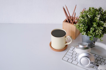 Office desk coffee mug, computer keyboard, pencil and headphone on table.