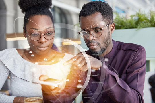 Film and visual effects. Black female and male hold modern digital device, message online, use futuristic technology with application interface, have serious facial expressions. Double exposure