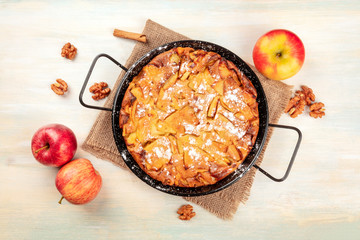 An apple pie in a pan, shot from above on a rustic wooden background with apples, cinnamon, walnuts and a place for text
