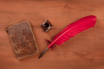 Writing Poetry. A photo of a red quill with and ink well and an old book, shot from the top on a dark wooden table with copy space