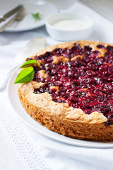 Homemade cherry pie served with cream on a light background with cherry leaves and flowers.