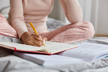Cropped image of unrecognizable woman in nightclothes, writes down information in notepad, rewrites...