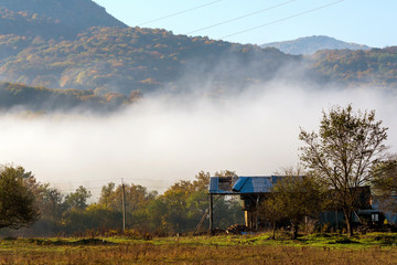 Old farm house in mountain in autumn foggy morning. Mountain village and old farm in the mountains. Clouds of fog and sky at background