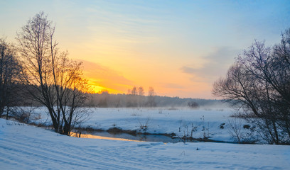 Fototapeta na wymiar Frosty foggy winter landscape with small forest river and rising sun.