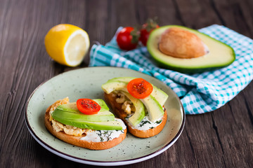 Toasts with avocado pieces, cherry tomatoes, scrambled eggs and soft cream cheese.