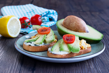 Toasts with avocado pieces, cherry tomatoes, scrambled eggs and soft cream cheese.