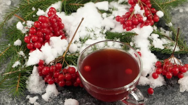 Winter still life with hot tea with viburnum berries, branch of pine and burning candle on the surface with hoarfrost and snow