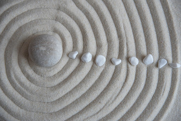 Fototapeta na wymiar Gray zen stones on the sand with wave drawings. Concept of harmony, balance and meditation, spa, massage, relax