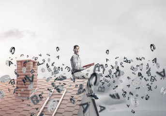 Fototapeta premium Man on brick roof reading book and symbols flying around