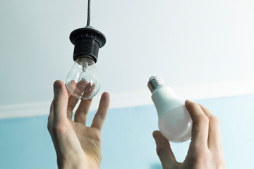 Incandescent lamp is changed to LED light by the hands of a man. Energy saving.  - 235273541