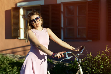 Fototapeta na wymiar portrait of a young, attractive girl in glasses and a pink dress on a bicycle