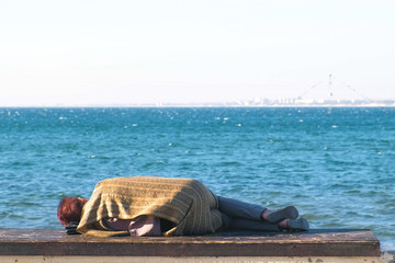 Homeless woman sleeping on a bench on the sea waterfront.