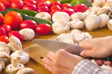 Woman's hands is cutting mushrooms champignons on the wooden bord on kitchen table.