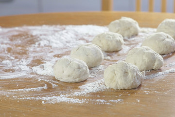 Yeast dough buns on the kitchen table with flour.
