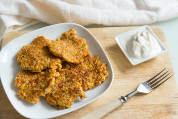 carrot pancakes on a white plate, fork, sour cream on a wooden Board