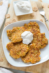 carrot pancakes on a white plate, fork, sour cream on a wooden Board, vegetable vegetarian pancakes