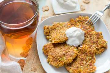 carrot pancakes on a white plate, fork, sour cream, black tea mug,
