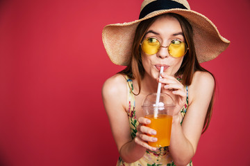 Portrair of happy and excited blond trendy woman in hat with fresh drink in hands isolated on pink...