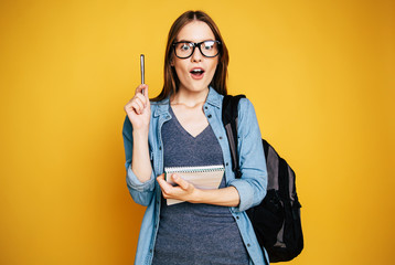 Happy and excited cute young student girl portrait in glasses with backpack isolated in studio