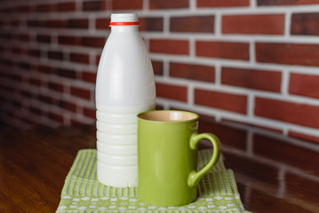 Still life a bottle of milk and a green ceramic mug, a green napkin on a wooden table, against the background of a red brick wall. Healthy foods.