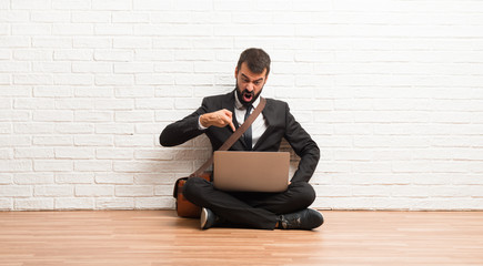 Businessman with his laptop sitting on the floor frustrated by a bad situation and pointing to the...