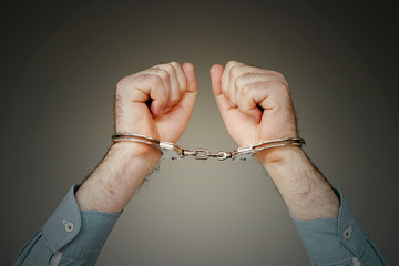 Close-up. Arrested man handcuffed hands isolated on gray background. Prisoner or arrested terrorist, close-up of hands in handcuffs.