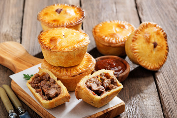 Traditional Australian Mini meat pies from shortbread dough on a wooden board over wooden background. © Nelea Reazanteva