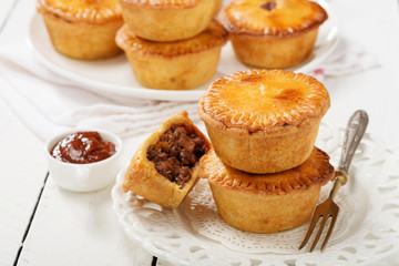 Traditional Australian Mini meat pies from shortbread dough on a white wooden background.