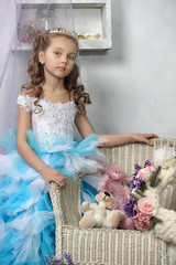 A girl in an elegant blue dress next to a chair with toys
