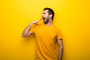 Man on isolated vibrant yellow color yawning and covering wide open mouth with hand