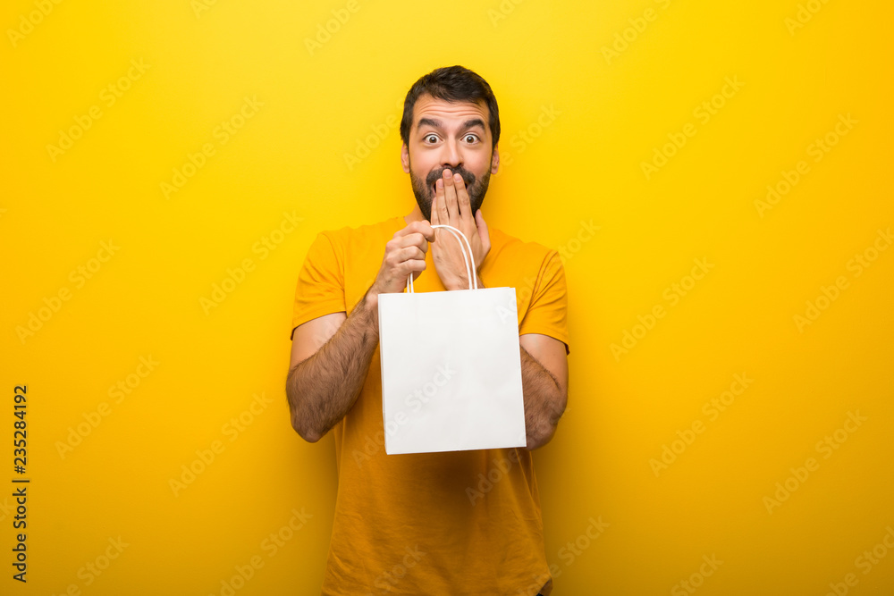 Wall mural man on isolated vibrant yellow color surprised while holding a lot of shopping bags