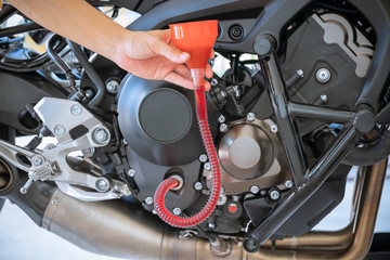Obraz premium Mechanic pouring Fresh oil being poured during an oil change to the Motorcycle engine, Pouring oil lubricant motorbike from bottle by Flexible Plastic Funnel on mechanic hand.