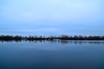 View across the river to the dark forest away in cold weather.