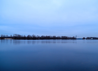 View across the river to the dark forest away in cold weather.