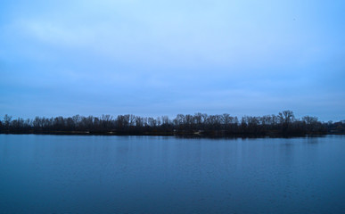 View across the river to the dark forest away in cold weather.