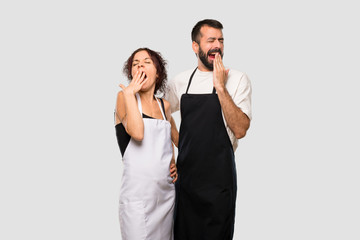 Couple of cooks yawning and covering mouth with hand. Sleepy expression on grey background