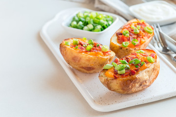 Baked loaded potato skins with cheddar cheese and bacon on ceramic plate, garnished with scallions and sour cream, horizontal, copy space