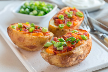 Baked loaded potato skins with cheddar cheese and bacon on ceramic plate, garnished with scallions and sour cream, horizontal
