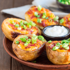 Baked loaded potato skins with cheddar cheese and bacon, garnished with scallions and sour cream, on a wooden plate, square format