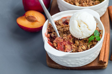 Plum crumble pie or plum crisp with oats and spices, served with vanilla ice cream ball, in baking dish, horizontal
