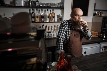 Brutal young barista in an apron tasting coffee at the bar in a modern cafe