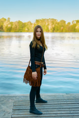 portrait of beautiful girl in full growth standing on the dock. woman is holding a bag on her shoulde © Olek