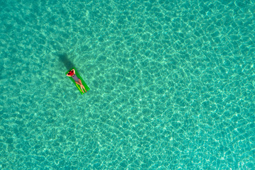 Aerial view of slim woman swimming on the swim mattress in the transparent turquoise sea in Seychelles. Summer seascape with girl, beautiful waves, colorful water. Top view from drone