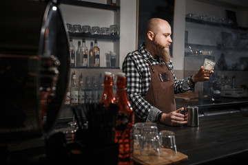 Brutal young barista in an apron tasting coffee at the bar in a modern cafe