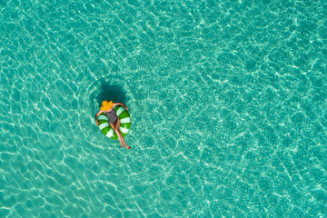 Aerial view of slim woman swimming on the swim ring  donut in the transparent turquoise sea in Seychelles. Summer seascape with girl, beautiful waves, colorful water. Top view from drone